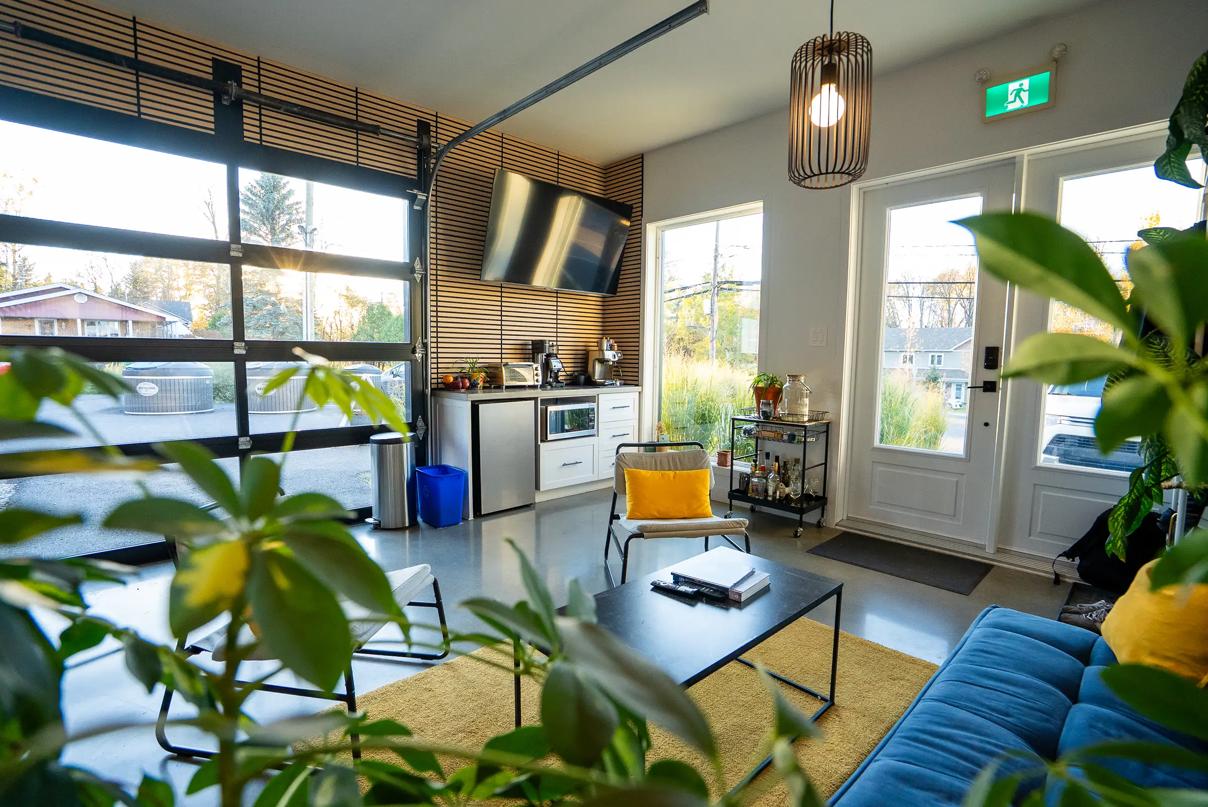 Le salon du Stoud vu à travers une plante, vers l’entrée et le coin café