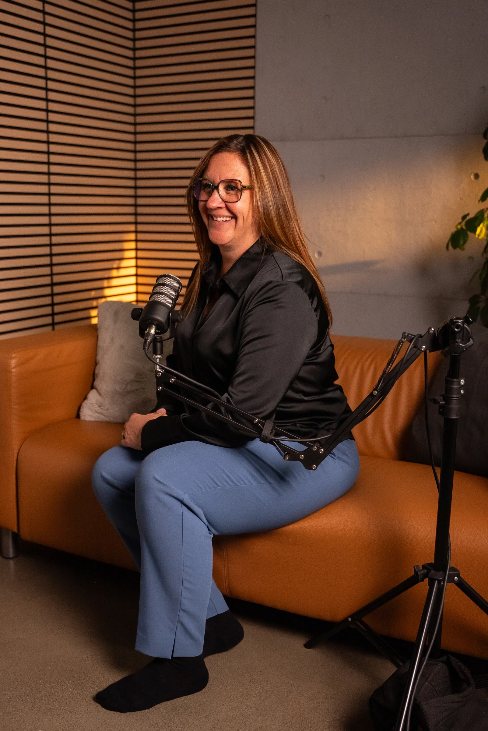 Une invitée assise sur le divan du studio podcast, devant le mur de lattes de bois