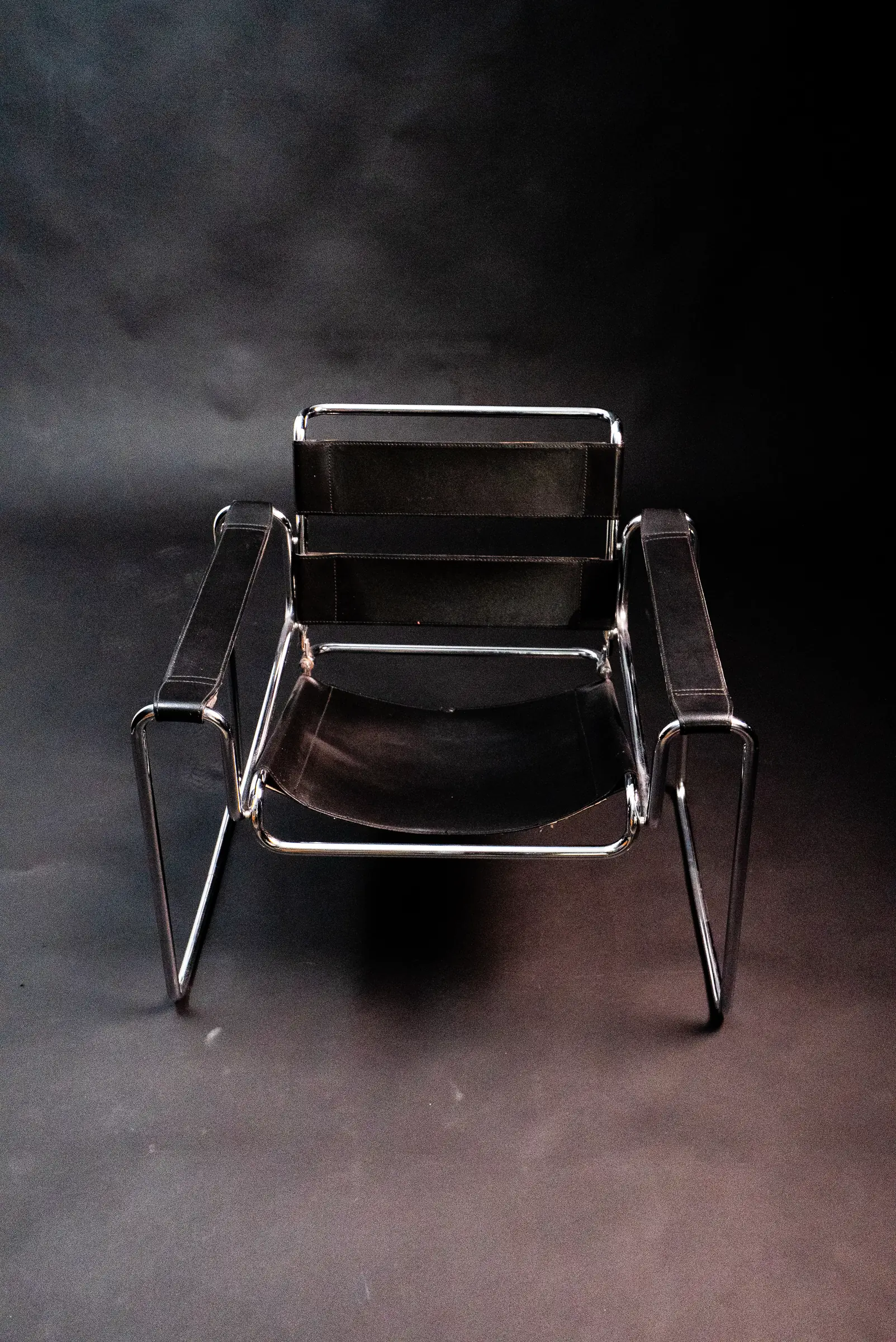 Une chaise en cuir et chrome sur le fond noir du studio photo, vue de trois quarts